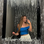 Woman in a blue top and white pants standing in front of a reflective surface with silver tinsel.