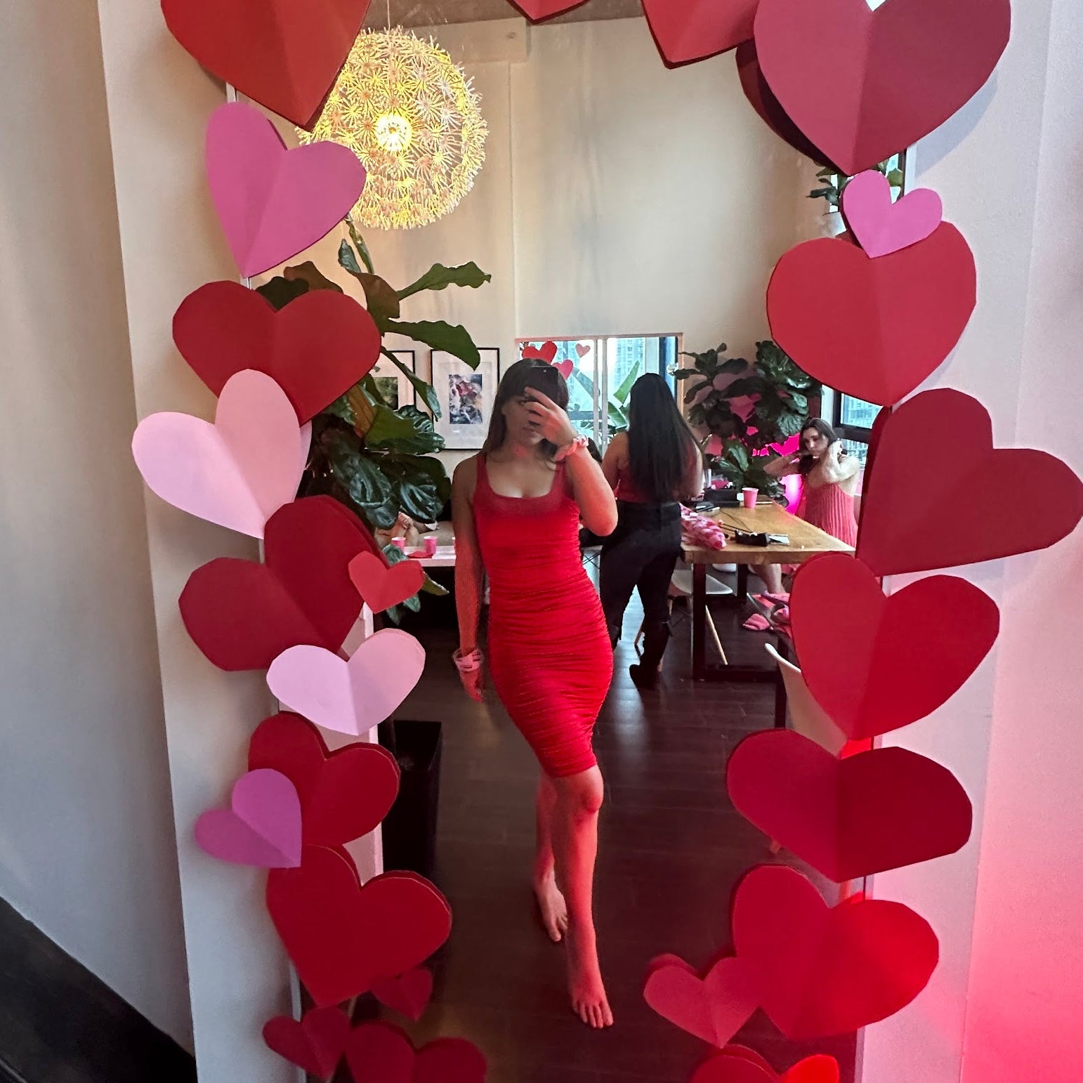 Woman in a red dress standing in front of a heart-shaped mirror frame.