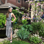 Woman in a zebra-striped dress standing in a garden with a pond and brick building in the background.