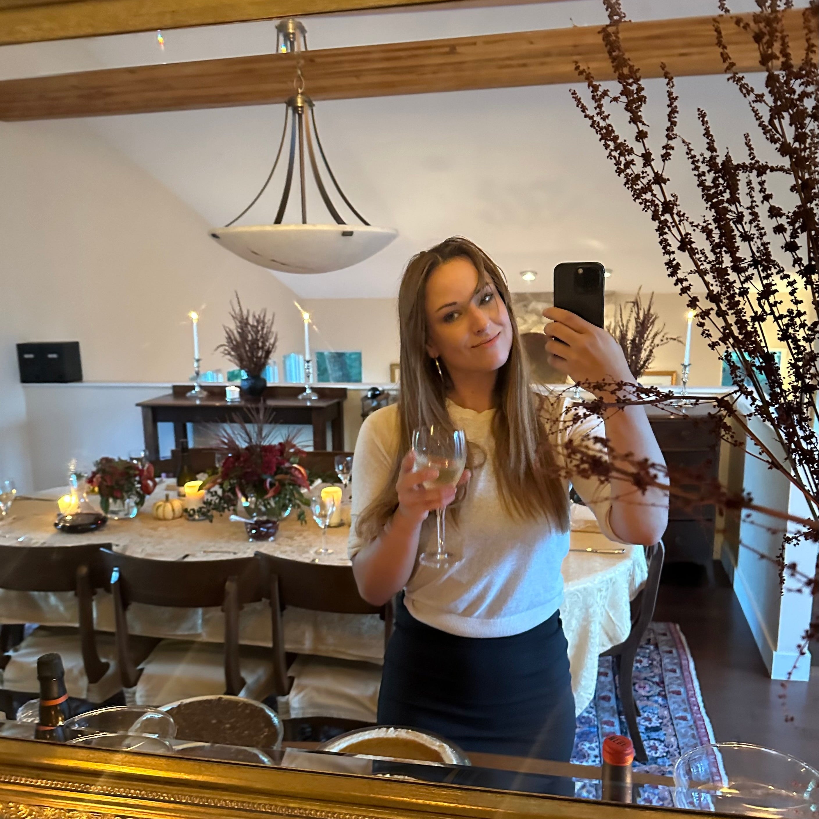 Woman taking a mirror selfie in a dining room with a large gold-framed mirror.