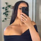 Woman taking a mirror selfie wearing a black off-shoulder dress in a bathroom wearing a diamond ring phone