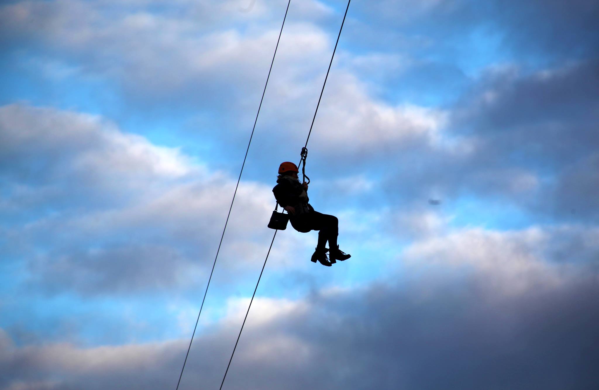 Person on a zip line against a blue sky with clouds