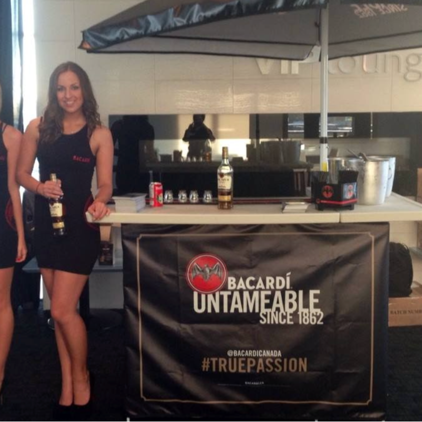 Woman holding a bottle under a Bacardi umbrella at an event.