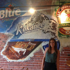 Woman standing in front of a mural featuring beer brand logos on a brick wall.