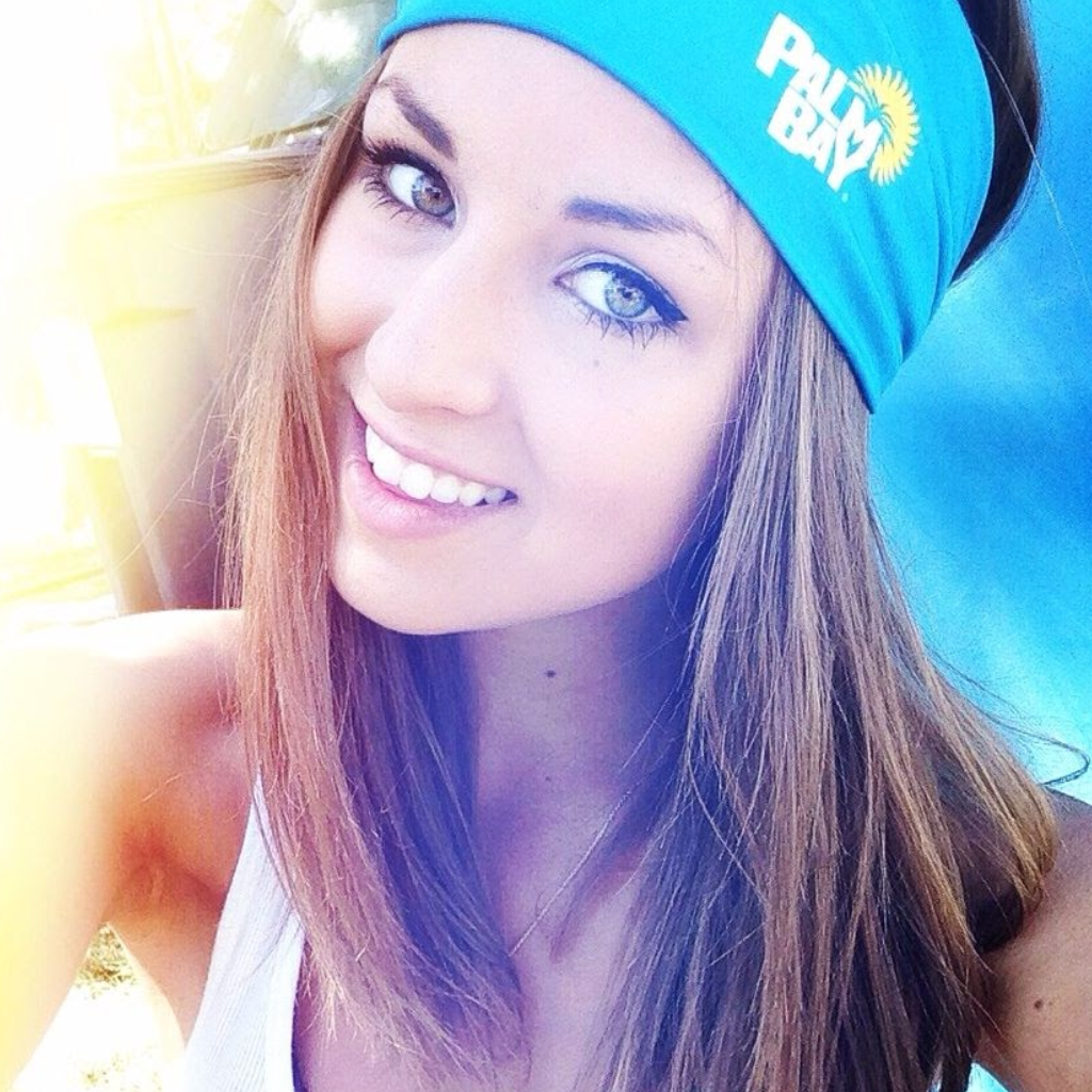 Woman wearing a blue headband with a logo, smiling outdoors.