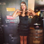 Woman in a black dress posing next to a barrel with 'Sleeman' branding in a bar setting.